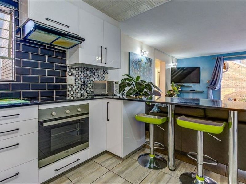 Open-plan kitchen and living area featuring modern white cabinetry, a breakfast bar, tiled backsplash, and integrated oven with extractor fan.