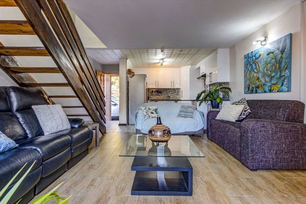 Open-plan living area featuring a wooden staircase, tiled flooring, and a compact kitchen with built-in cabinetry and a tiled backsplash.