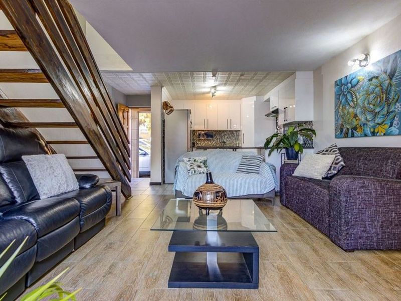 Open-plan living area featuring a wooden staircase, tiled flooring, and a compact kitchen with built-in cabinetry and a tiled backsplash.