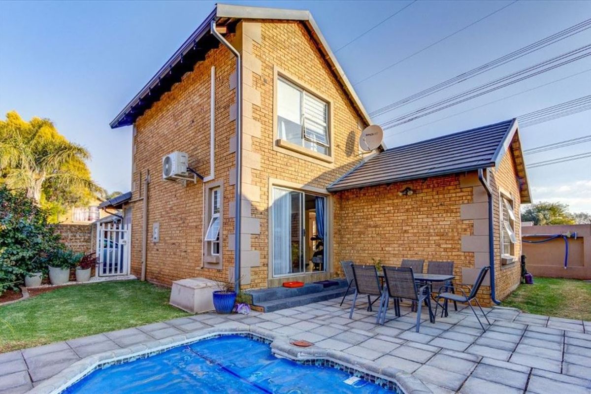Rear view of a brick townhouse featuring a paved patio area, swimming pool, and sliding door access to the interior.