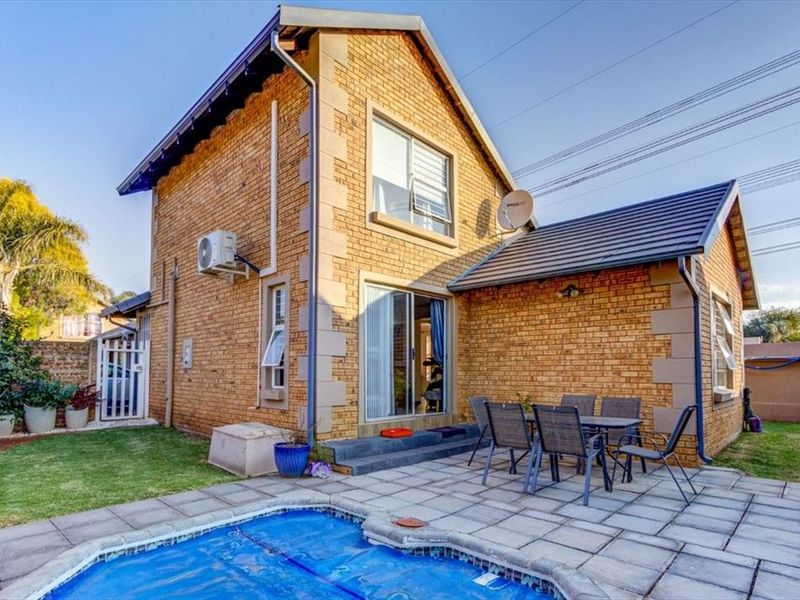 Rear view of a brick townhouse featuring a paved patio area, swimming pool, and sliding door access to the interior.