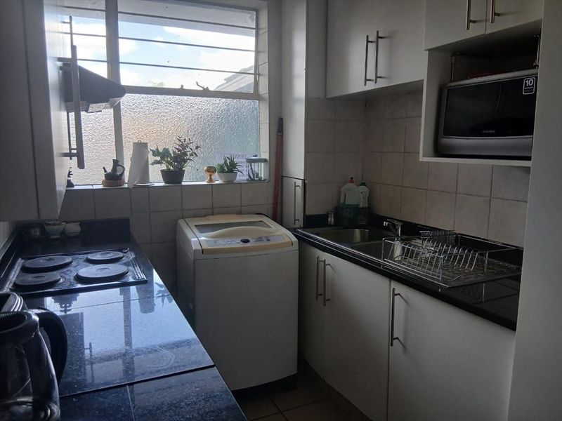 Compact kitchen featuring granite countertops, built-in cabinetry, electric hob, and tiled backsplash with integrated space for a washing machine.