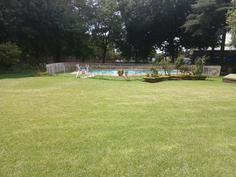 A well-maintained communal garden area featuring a fenced swimming pool surrounded by mature trees and manicured lawn.