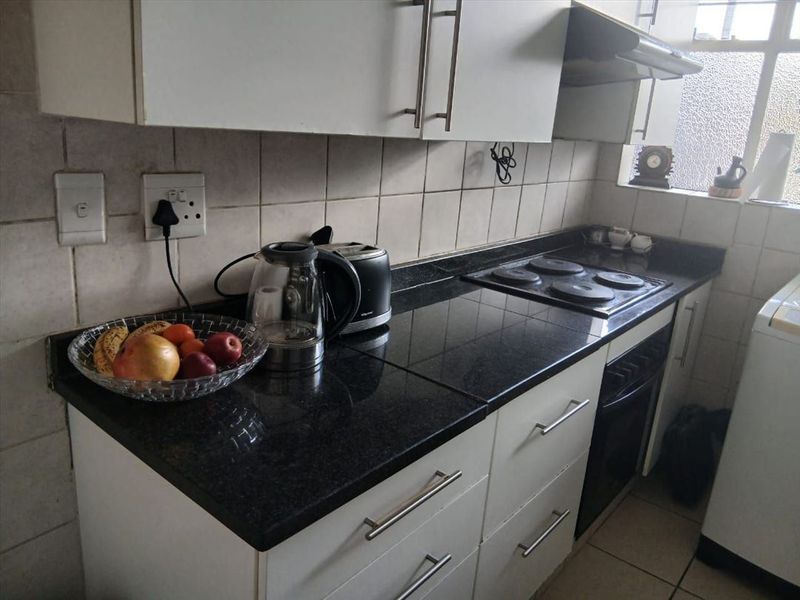 A functional kitchen featuring granite countertops, built-in oven, electric hob, extractor fan, and white cabinetry with tiled backsplash.