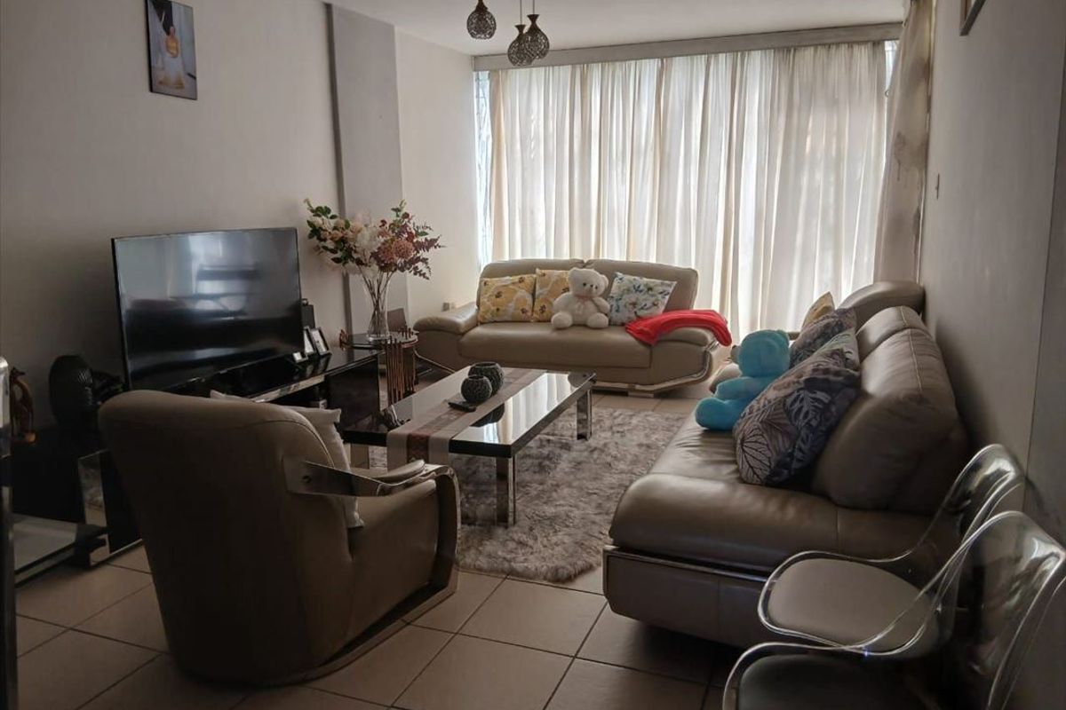 A comfortable living room featuring tiled flooring and large windows with floor-to-ceiling curtains, providing ample natural light.