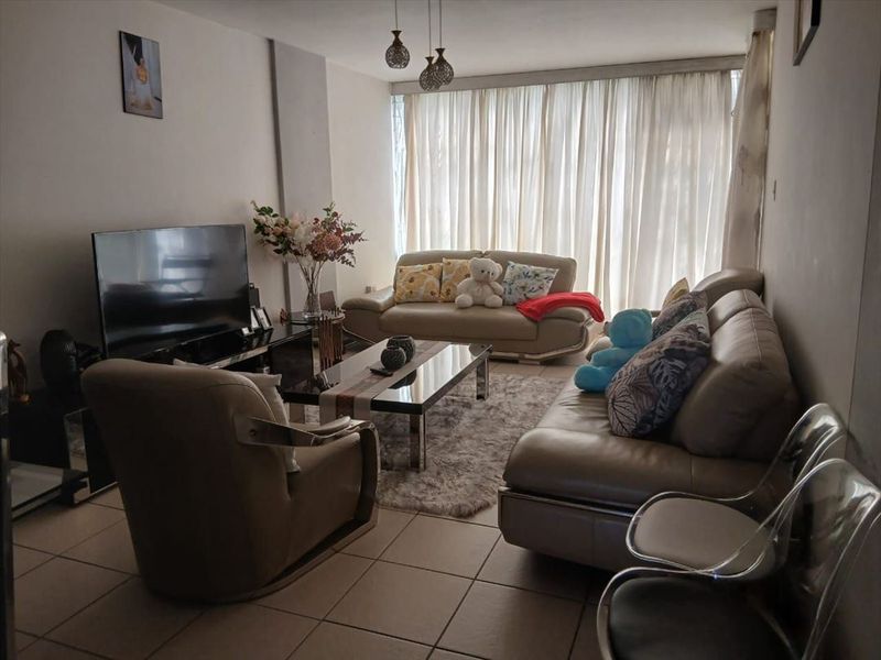 A comfortable living room featuring tiled flooring and large windows with floor-to-ceiling curtains, providing ample natural light.