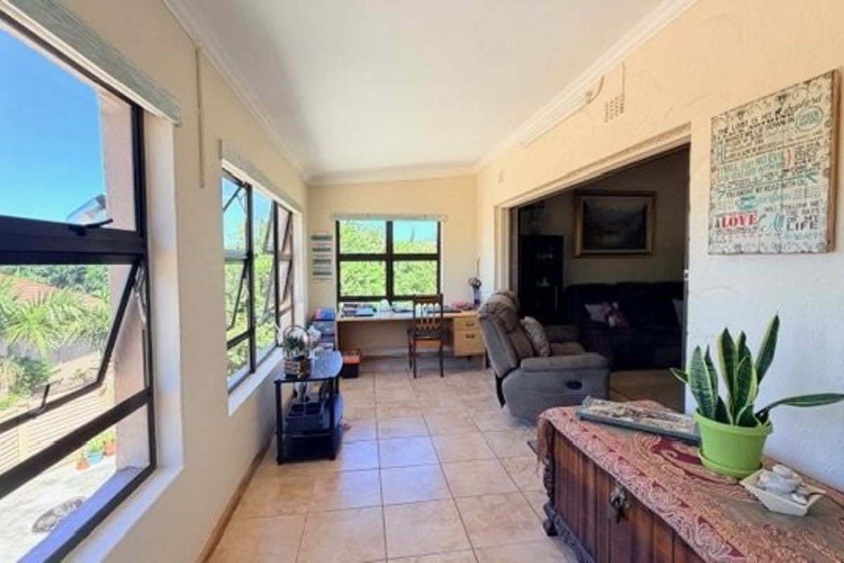 A sunlit living area featuring tiled flooring, large windows providing natural light, and direct access to the adjacent room.