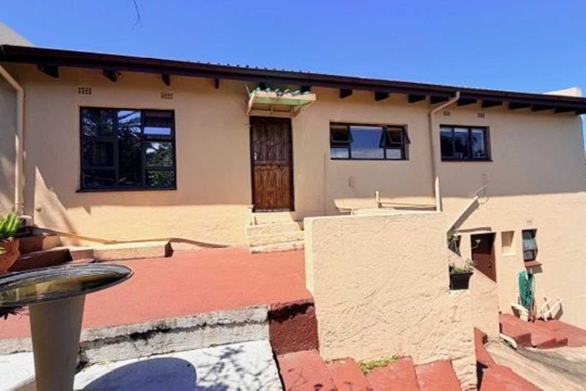 Rear elevation of the house featuring a terracotta-tiled patio area, exposed timber rafters, and aluminium window frames.
