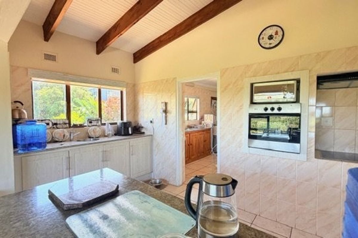 A functional kitchen featuring exposed timber ceiling beams, built-in oven and microwave, tiled splashbacks, and a central island, with an adjoining scullery area.