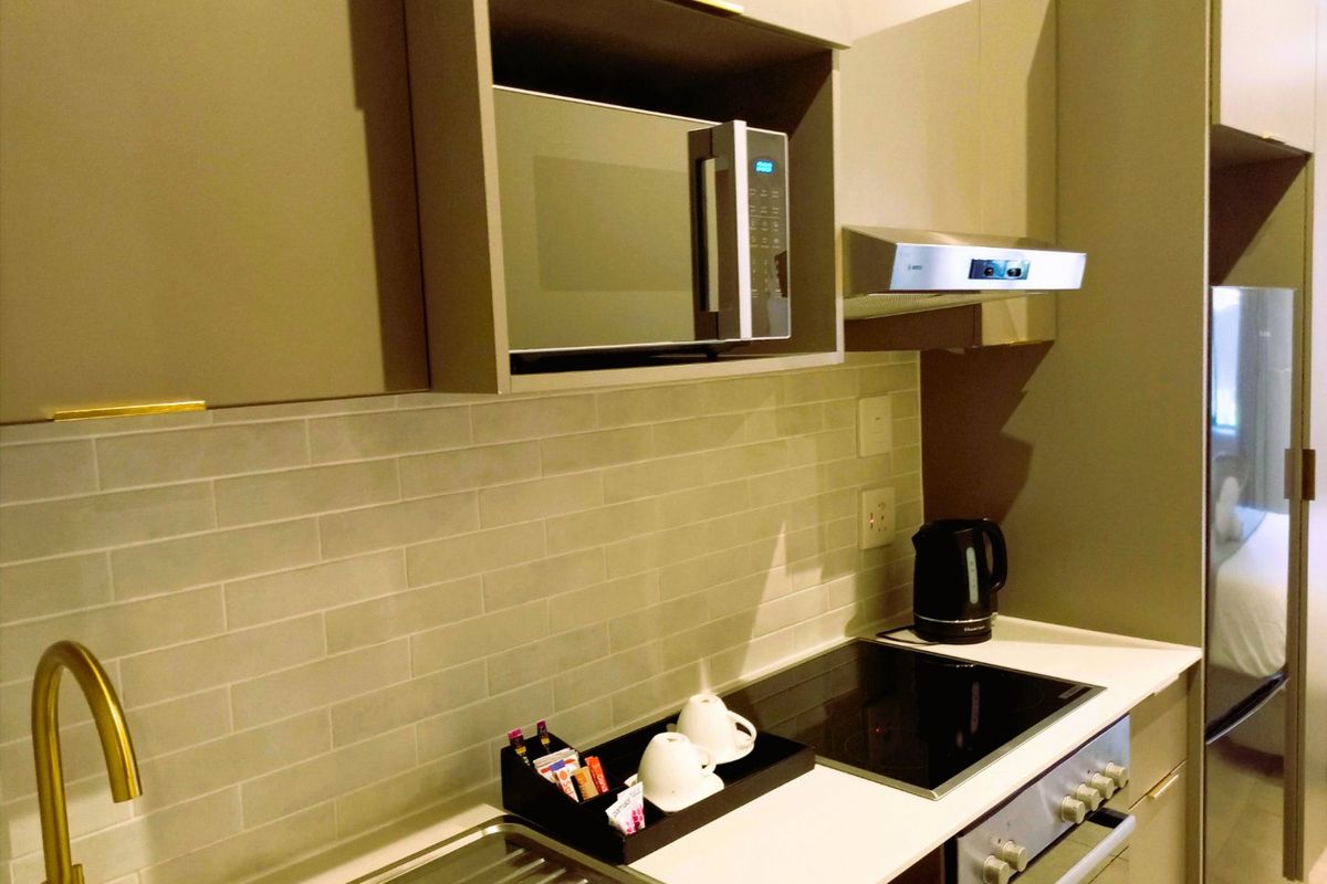 Modern kitchen featuring sleek cabinetry, subway tile backsplash, integrated microwave, electric hob, built-in oven, and a stylish brass faucet.