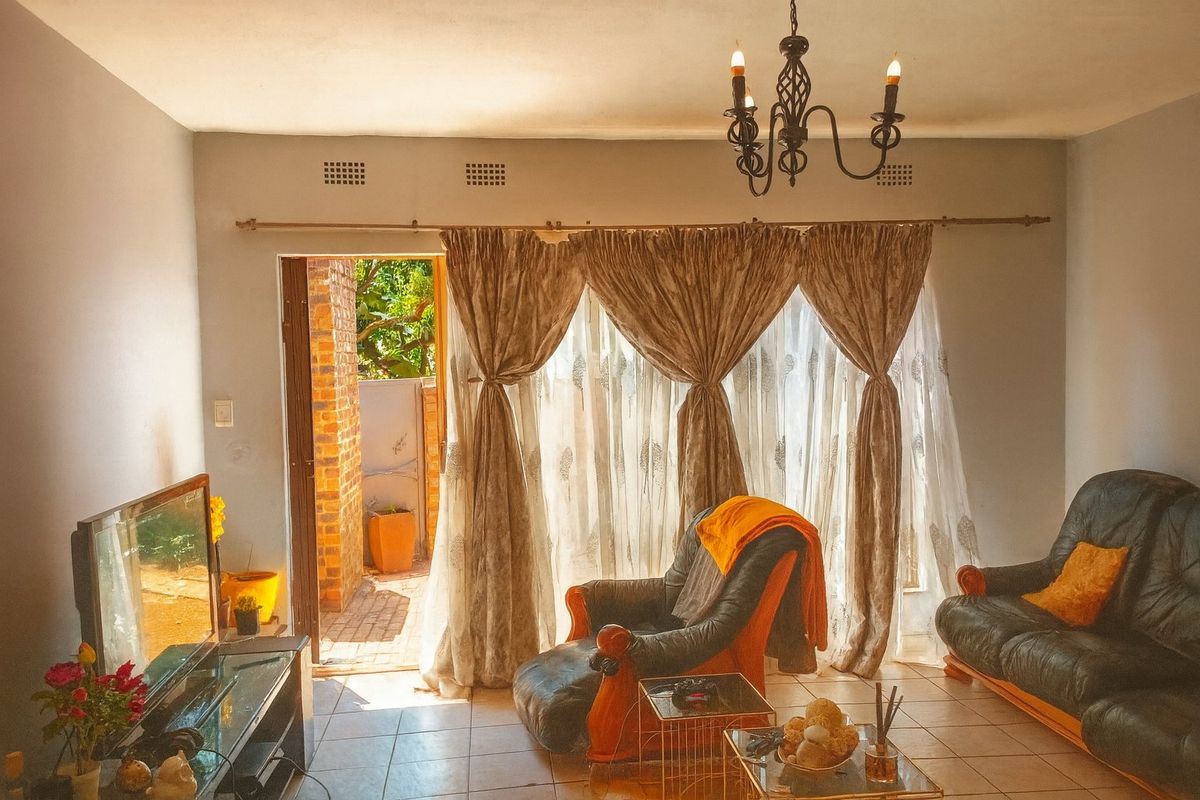 A living room featuring tiled flooring, a wrought iron chandelier, and a sliding door providing access to an outdoor patio area.