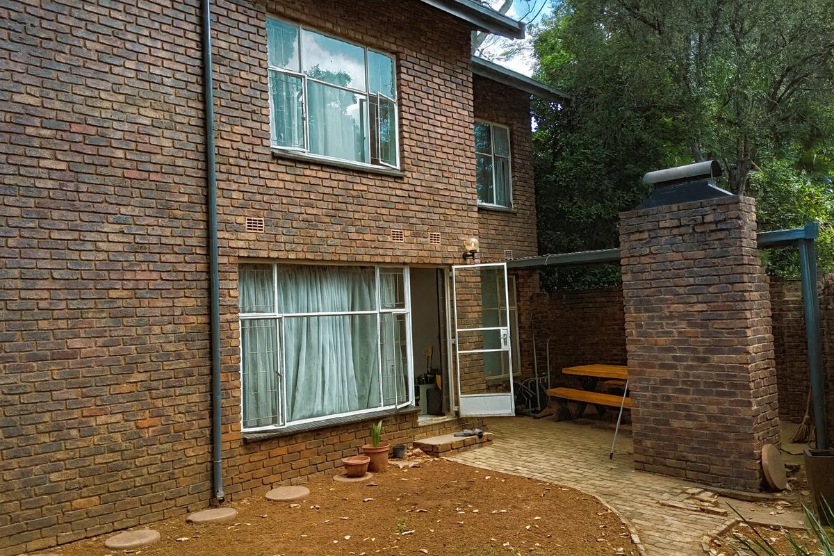 Rear view of a face brick townhouse featuring a paved patio area with a built-in brick braai and established garden surroundings.