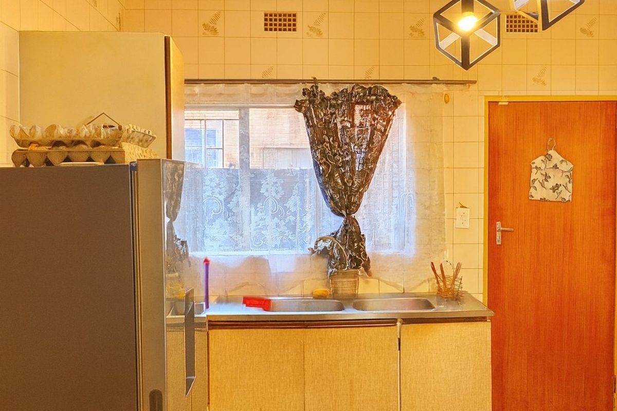 A functional kitchen featuring a double stainless steel sink, tiled splashback, and built-in cabinetry, offering potential for modern updates.