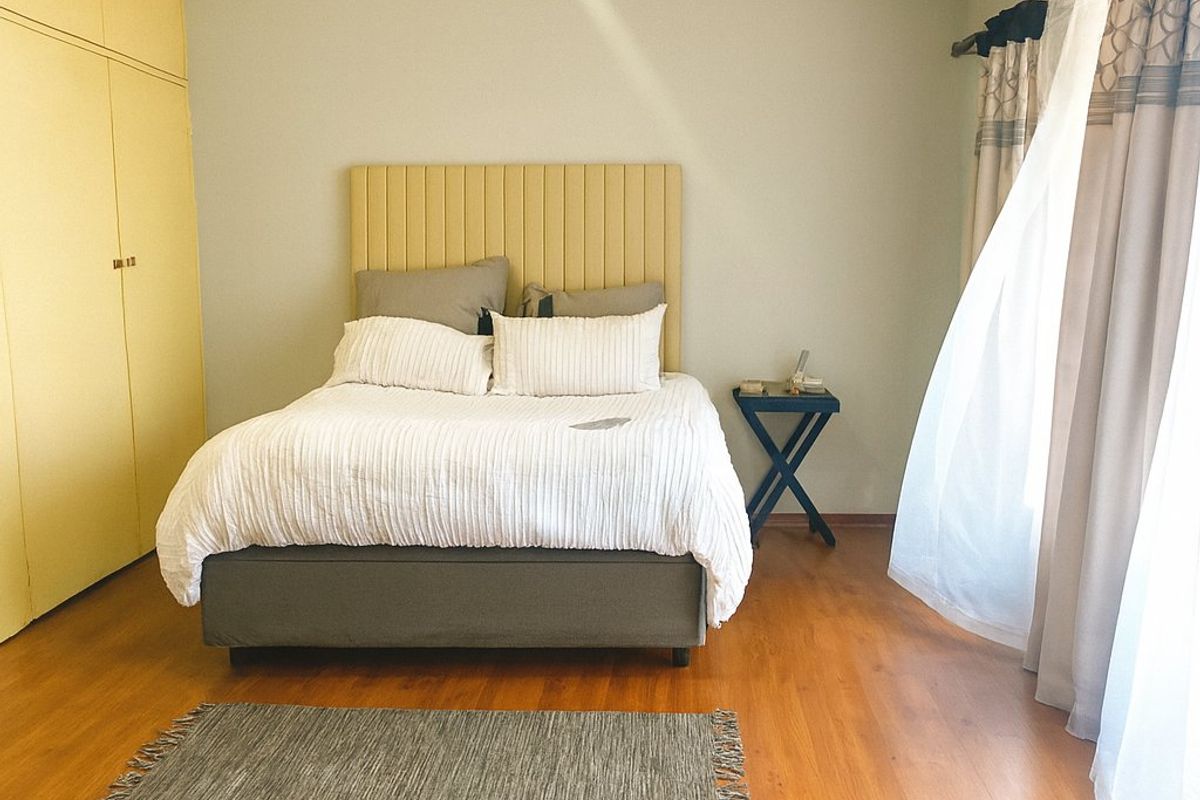 A well-lit bedroom featuring laminate flooring, built-in cupboards, and large windows with curtain rails.