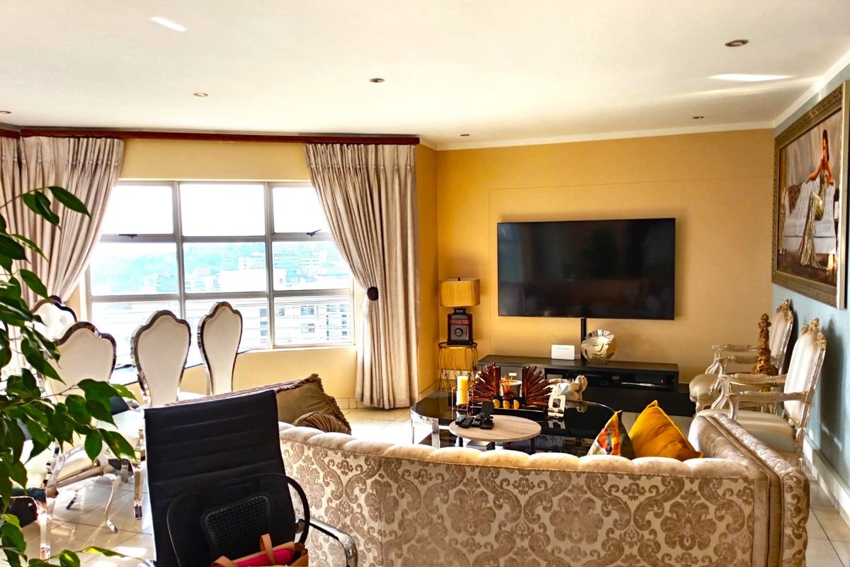 A well-lit living room featuring large windows with natural light, tiled flooring, and recessed downlighting, creating a comfortable and inviting atmosphere.