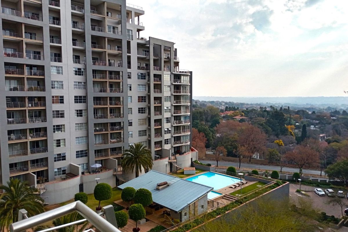 Aerial view of a modern apartment complex featuring a swimming pool, landscaped garden areas, and private balconies for each unit.