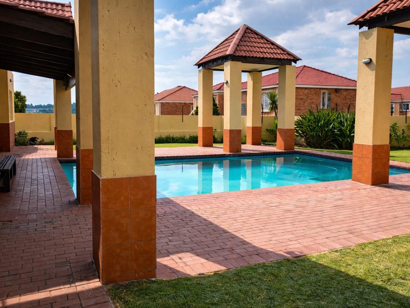 Outdoor pool area featuring a swimming pool, brick paved patio, and a covered pergola structure with tiled pillars.