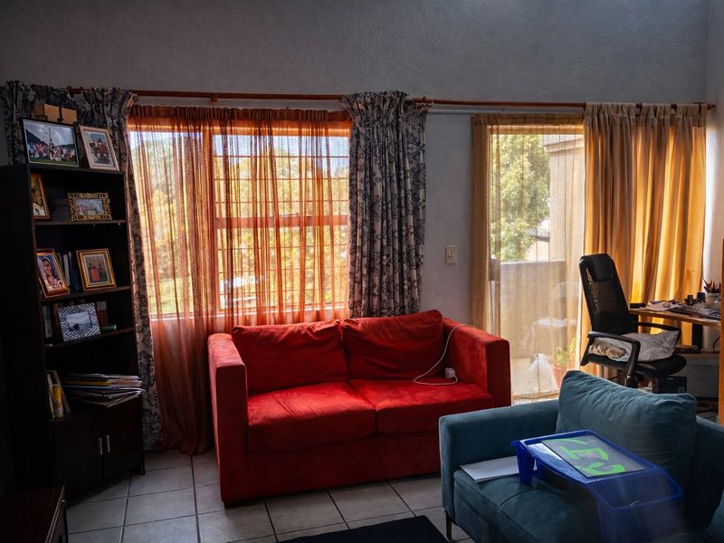 A living room area featuring tiled flooring, large windows, and a sliding glass door providing access to an outdoor space.