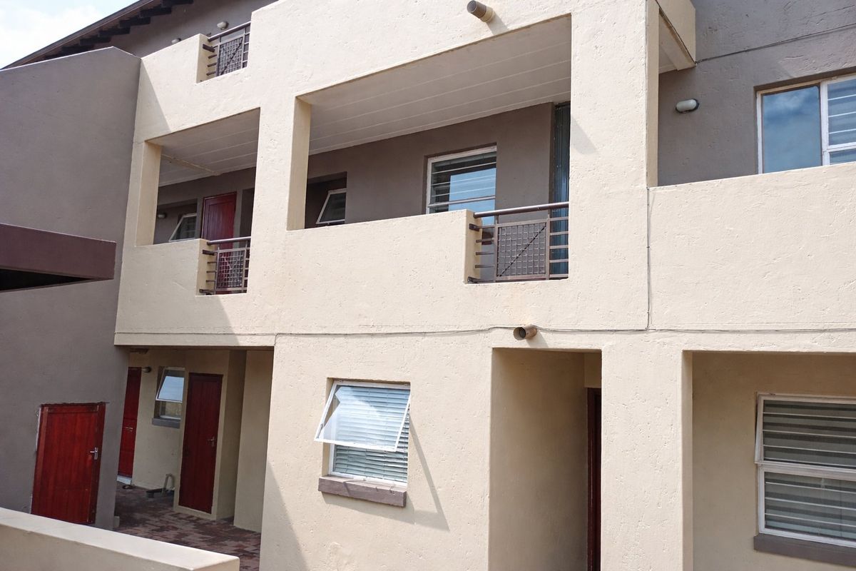 Rear elevation of an apartment complex featuring multi-level balconies, paved ground area, and standard casement windows.