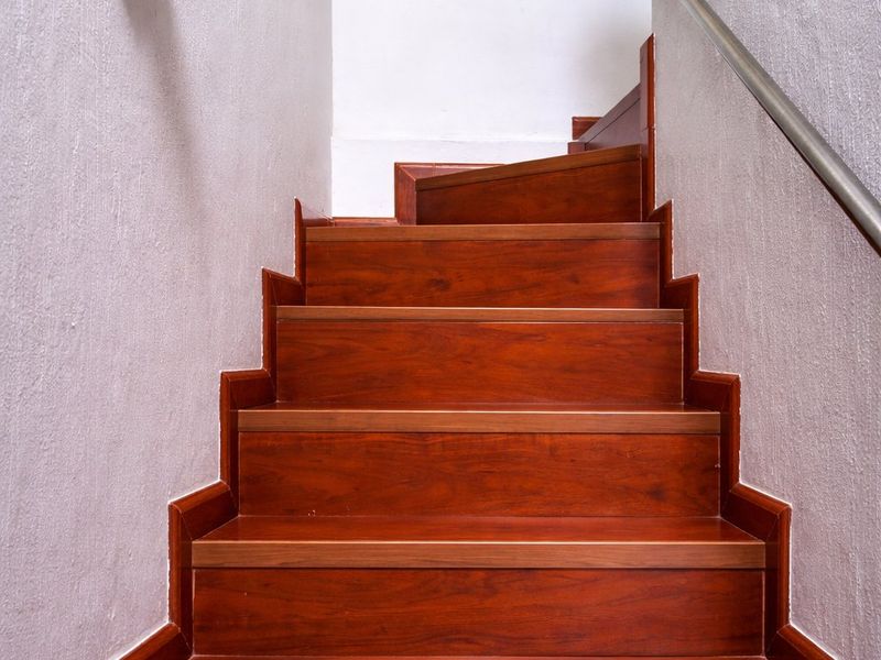 A well-maintained interior staircase featuring polished wooden treads and a sleek metal handrail, illuminated by a classic wall-mounted light fixture.