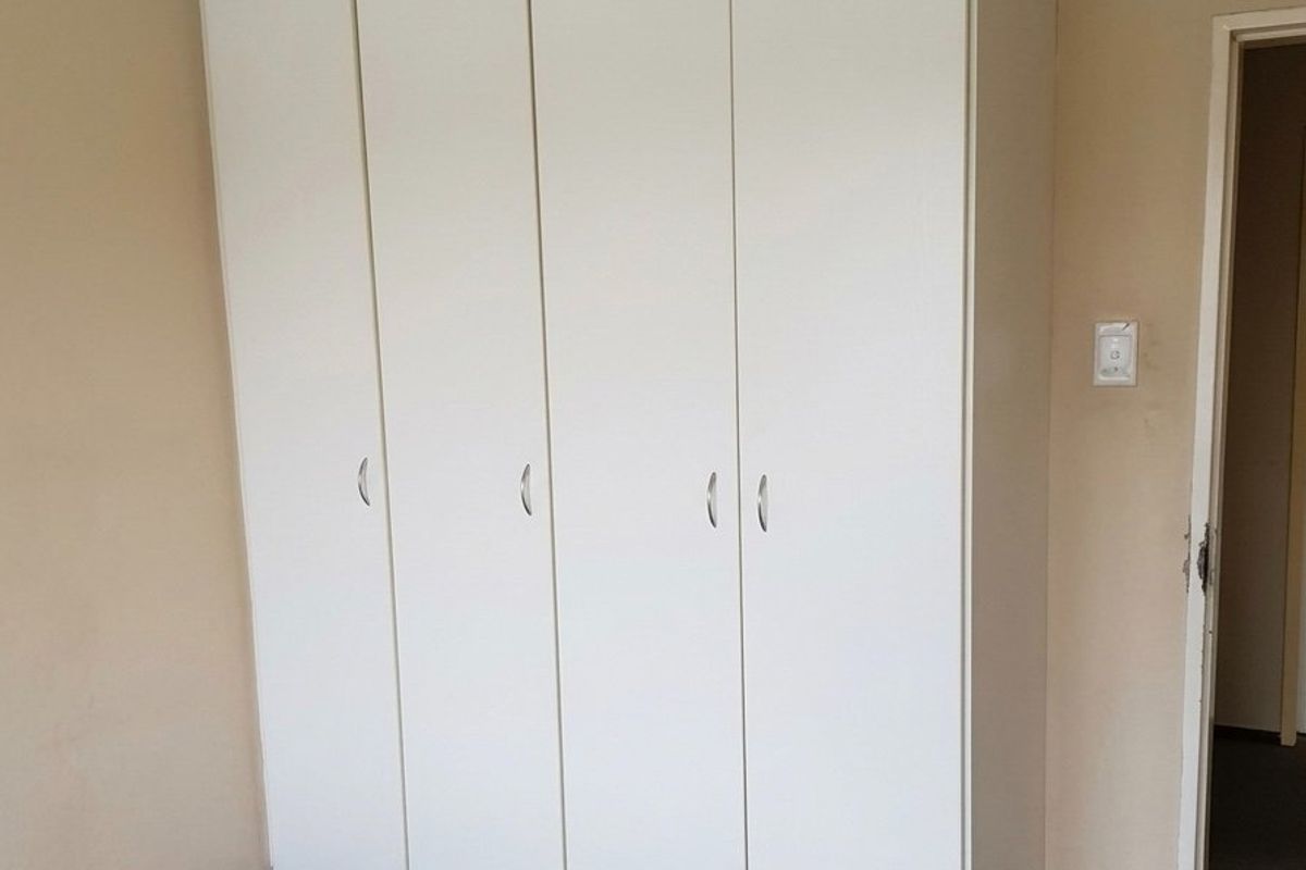 A bedroom featuring a large, white built-in wardrobe with modern handles and decorative crown molding.