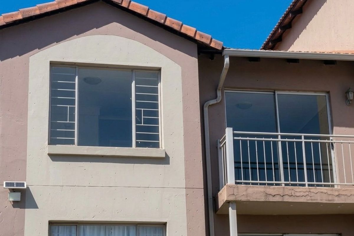 Exterior view of the apartment building featuring a balcony with metal balustrade, sliding glass doors, and security bars on the windows.