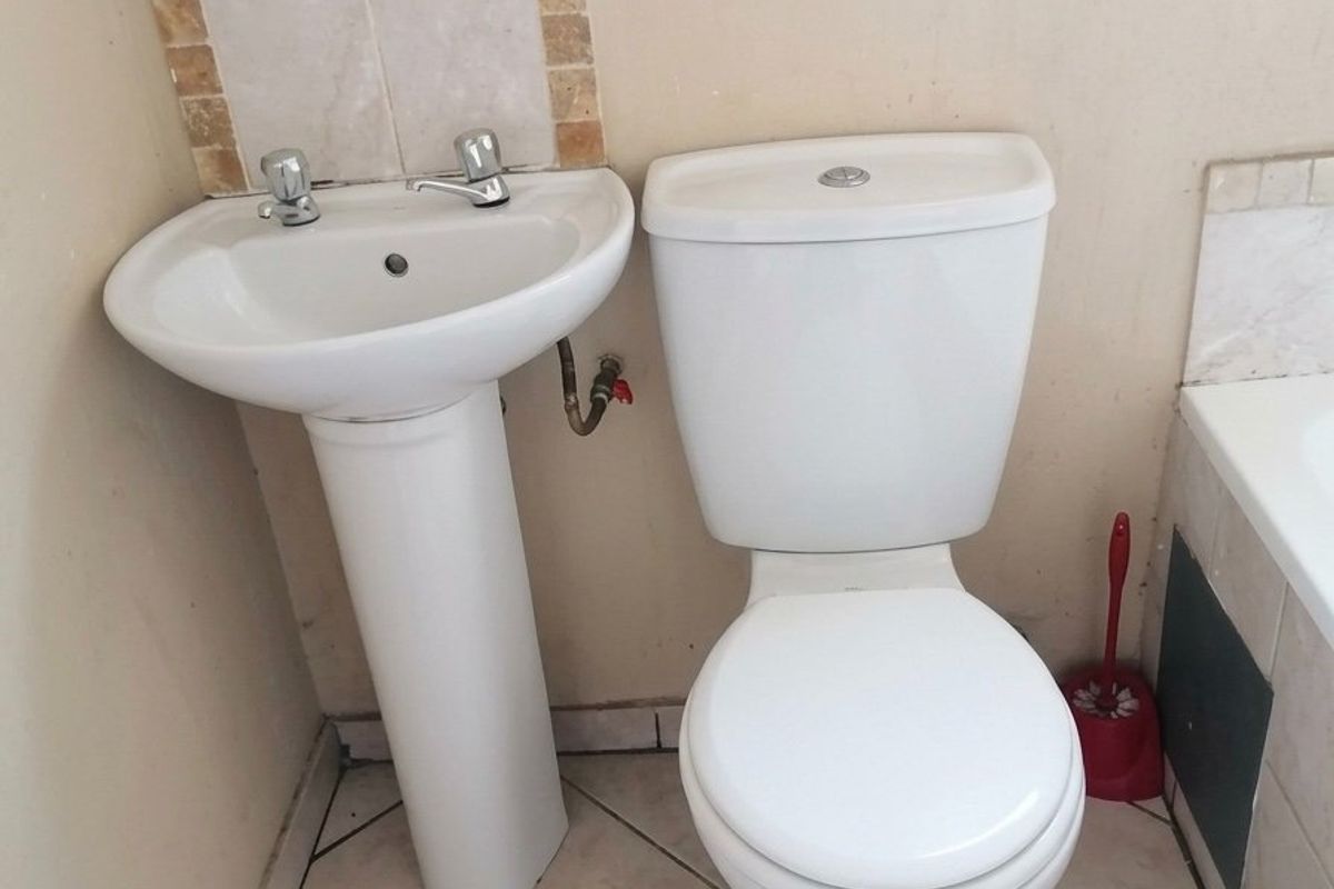 A compact bathroom featuring a pedestal basin, dual flush toilet, and tiled splashback, requiring cosmetic updates to improve the overall finish.