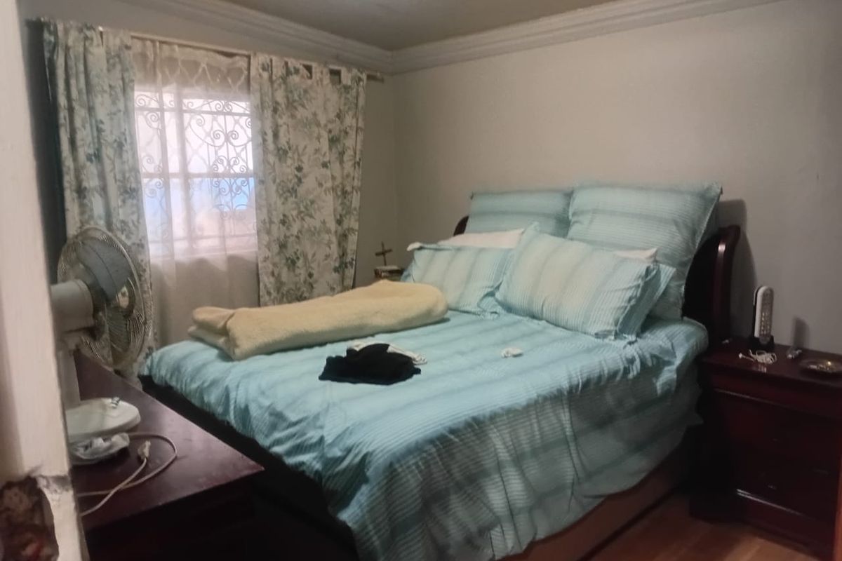 A bedroom featuring laminate flooring and a security gate on the window, showing signs of wear and requiring minor wall repairs.