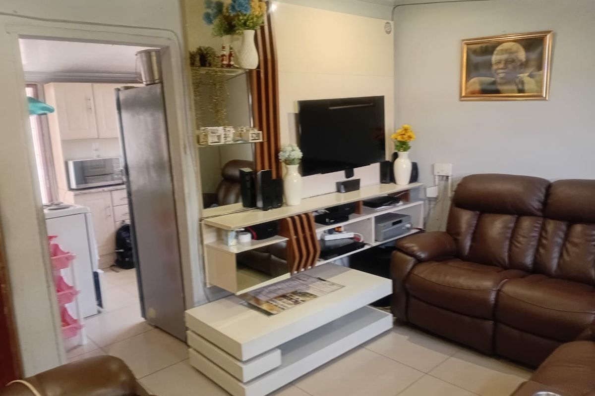 A comfortable living room featuring tiled flooring and a built-in media console, with an open transition into the adjacent kitchen area.