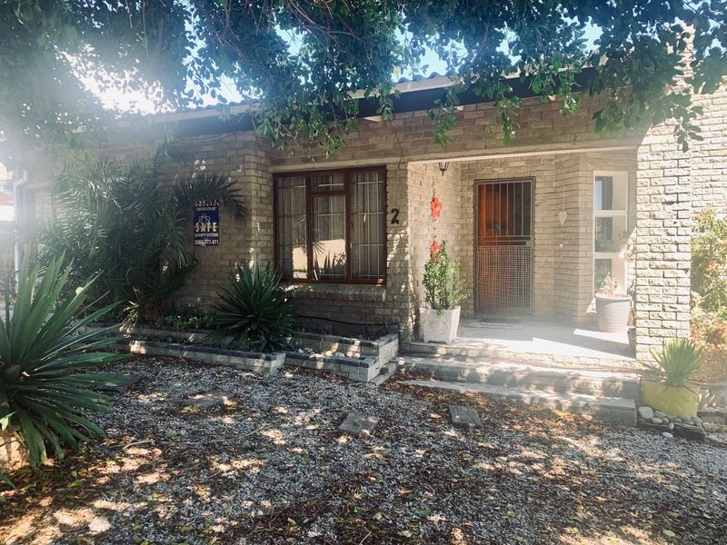 Front elevation of a face brick house featuring a covered entrance porch, security gate, and a gravel driveway with established garden beds.