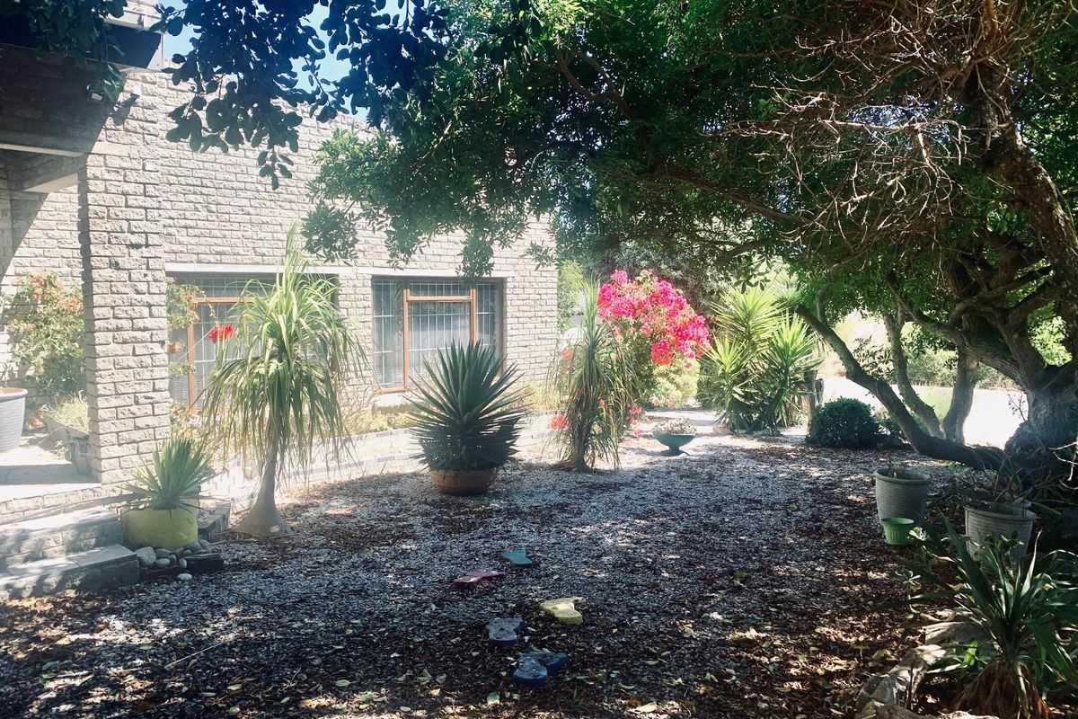A view of the rear garden featuring a brick facade, mature trees, and established landscaping.