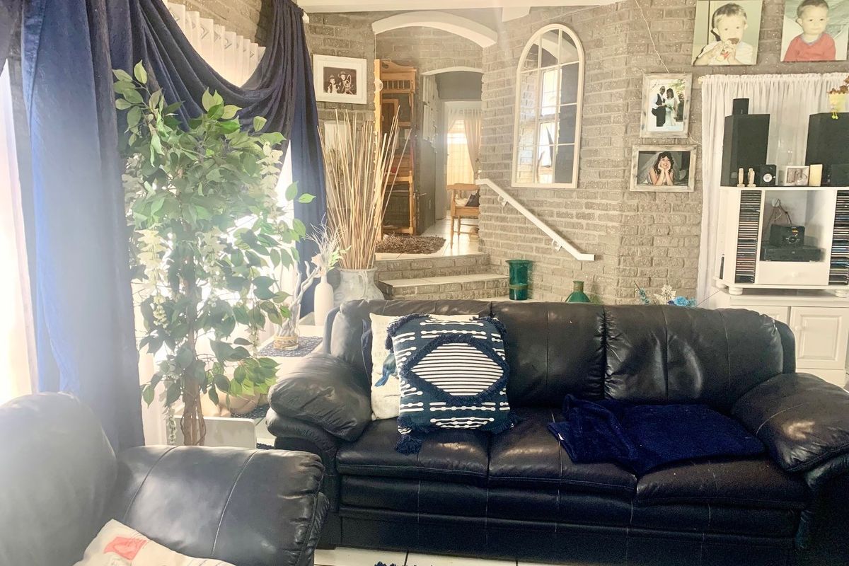 A living room featuring exposed brick walls, tiled flooring, and an arched transition leading to an elevated hallway area.