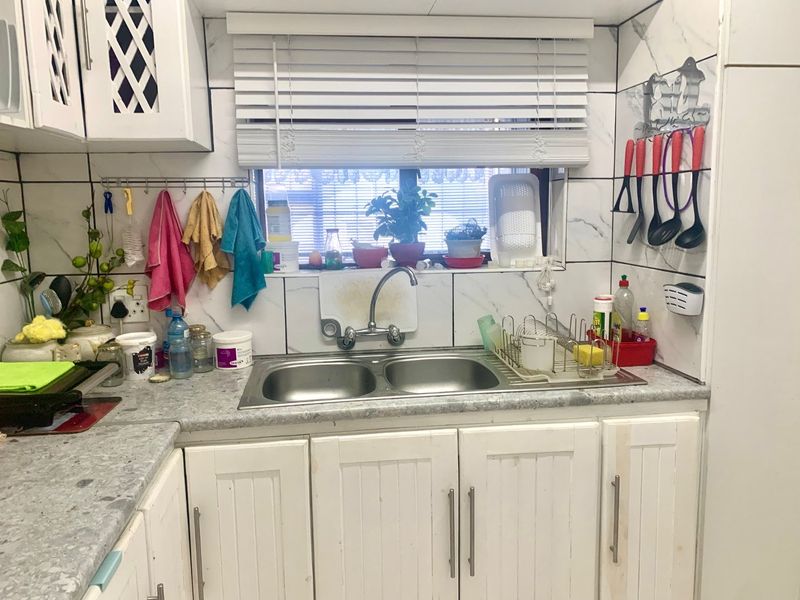 A functional kitchen area featuring white cabinetry, a double stainless steel sink, and marble-look wall tiling.