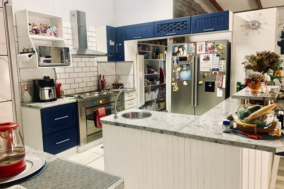 Spacious kitchen featuring blue and white cabinetry, stone countertops, a stainless steel gas stove, and an integrated walk-in pantry with subway tile backsplash.
