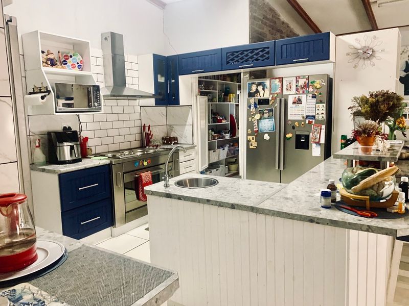 Spacious kitchen featuring blue and white cabinetry, stone countertops, a stainless steel gas stove, and an integrated walk-in pantry with subway tile backsplash.