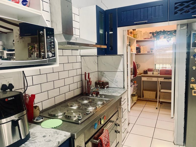 A functional kitchen featuring blue cabinetry, stainless steel stove, subway tile backsplash, and an adjoining scullery area with additional storage.