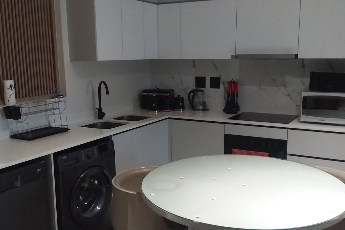 Modern kitchen featuring sleek white cabinetry, marble-look splashback, stone countertops, integrated appliances, and a functional layout with a dedicated laundry area.