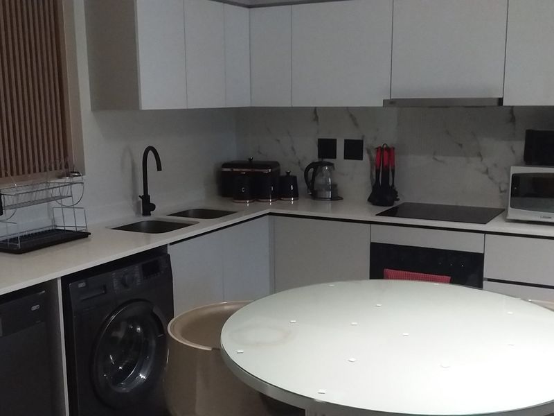 Modern kitchen featuring sleek white cabinetry, marble-look splashback, stone countertops, integrated appliances, and a functional layout with a dedicated laundry area.