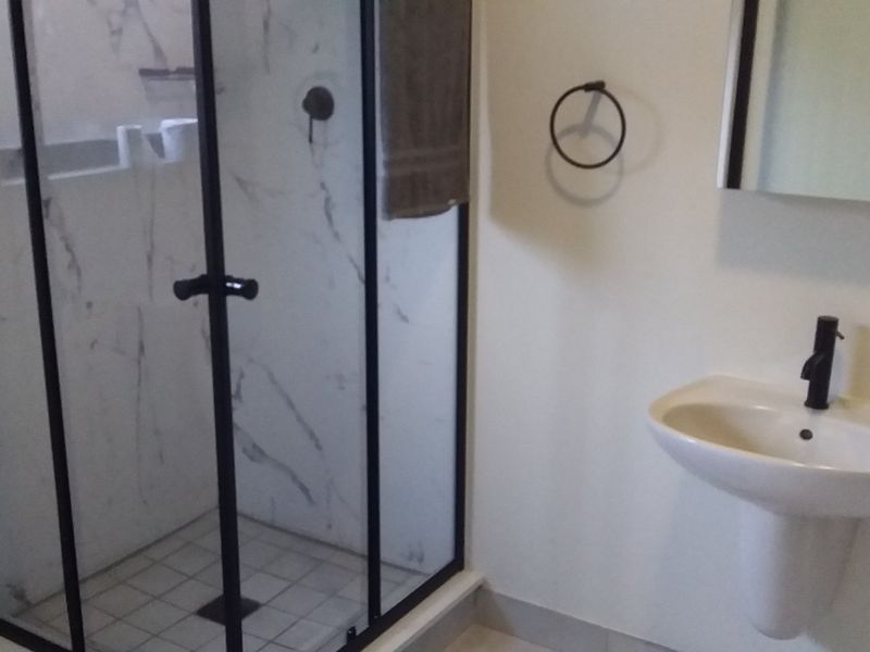 A modern bathroom featuring a glass-enclosed shower with marble-look tiling, black fixtures, and a pedestal basin.
