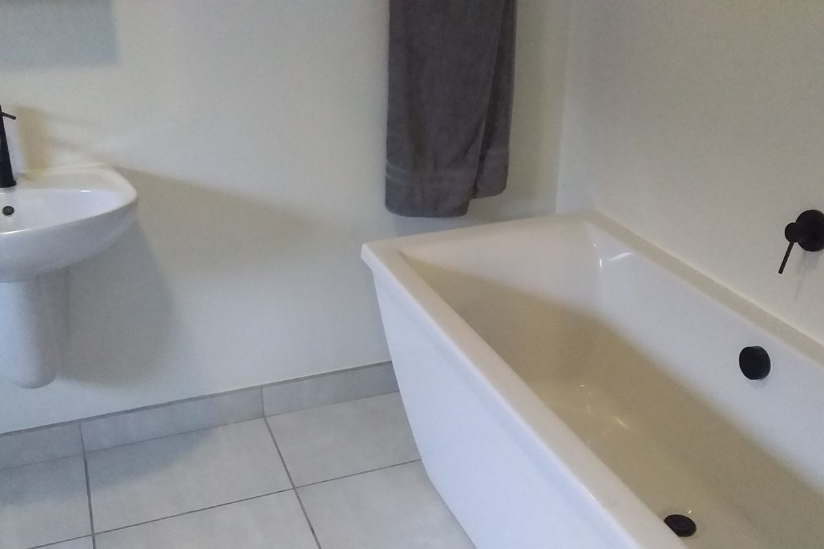 A clean, modern bathroom featuring a white pedestal basin with black tapware and a matching freestanding bathtub with wall-mounted black fixtures.