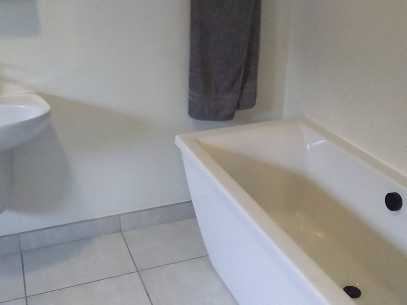 A clean, modern bathroom featuring a white pedestal basin with black tapware and a matching freestanding bathtub with wall-mounted black fixtures.