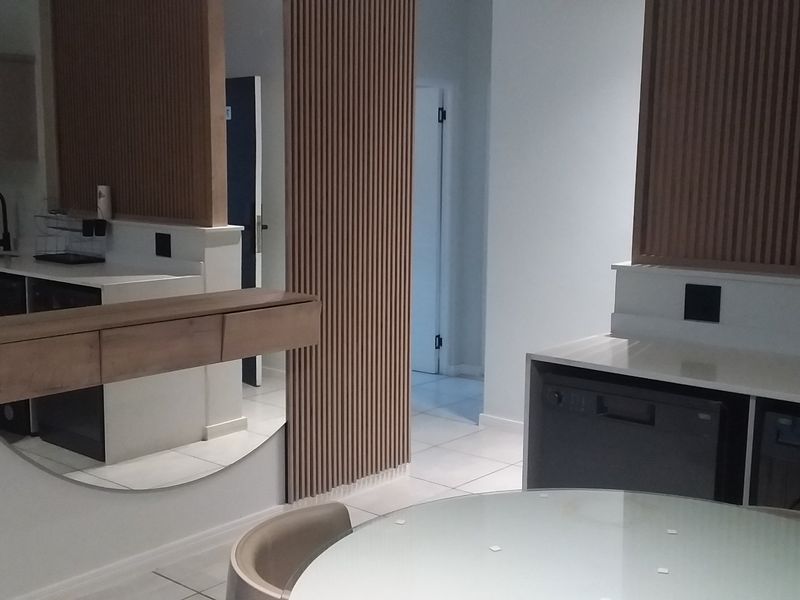 Modern kitchen featuring sleek white cabinetry, stone countertops, and stylish slatted timber wall paneling, creating a contemporary and functional culinary space.