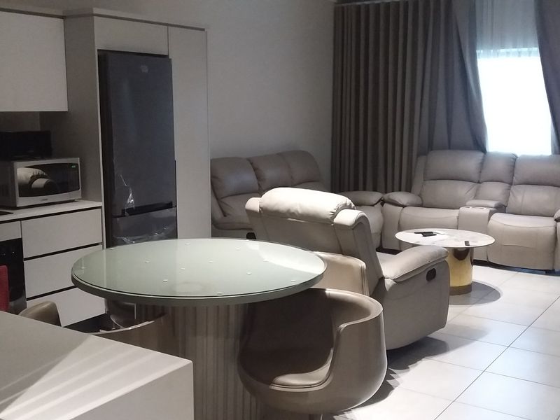 Modern open-plan living area featuring a sleek kitchen with integrated appliances and tiled flooring, seamlessly flowing into a comfortable lounge space.