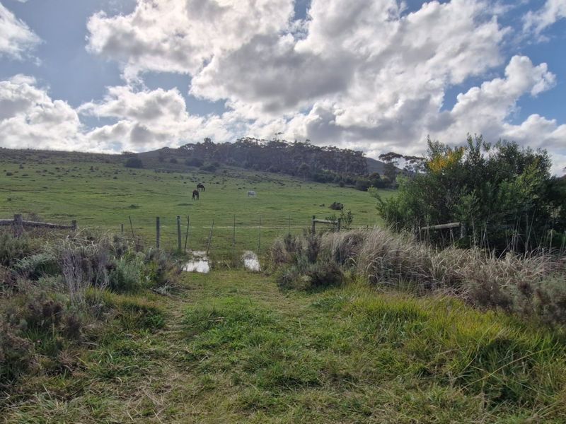 A scenic view of the expansive farm pasture with wire fencing and rolling hills under a cloudy sky.