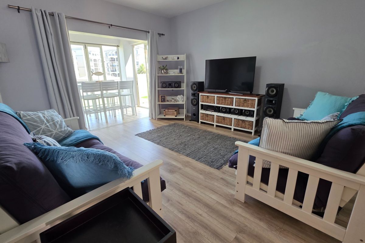A bright and inviting living room featuring light wood-look flooring, neutral walls, and large sliding glass doors that open onto a patio area.