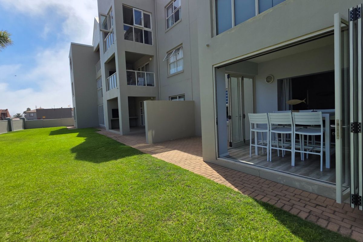 Exterior view of the apartment building featuring a paved patio area with folding glass doors leading to an open-plan living space and garden.