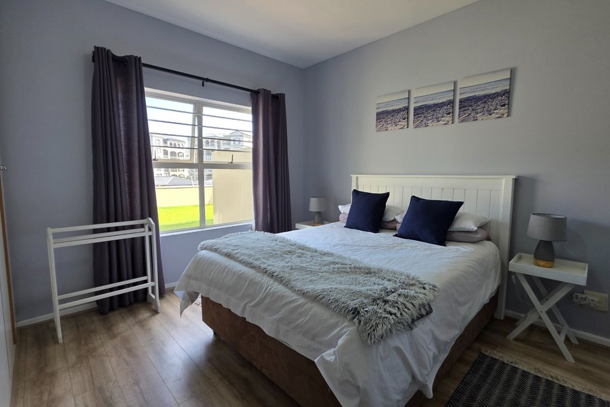 A well-maintained bedroom featuring light wood-look flooring, built-in wardrobe, and a window with security bars, offering a clean and comfortable living space.