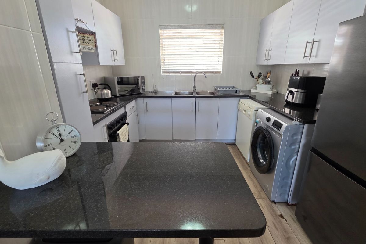 A functional kitchen featuring white cabinetry, dark granite countertops, a double sink, and integrated space for laundry appliances.