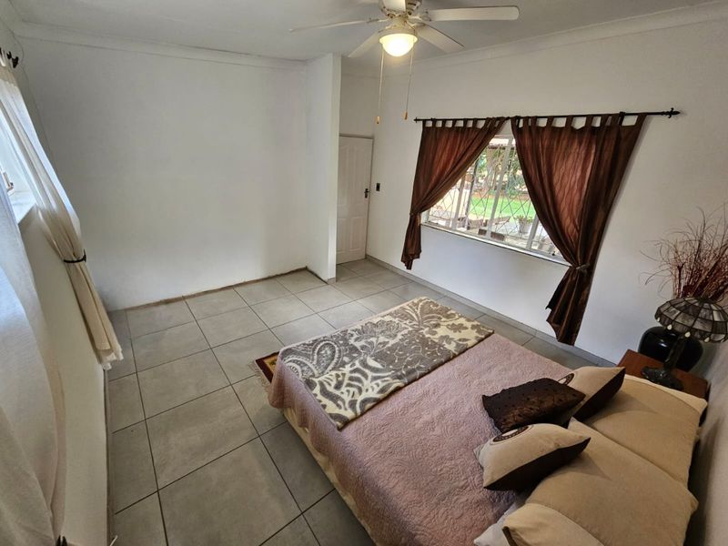 A bedroom featuring tiled flooring, a ceiling fan, and a window with security bars, offering a functional and well-lit living space.