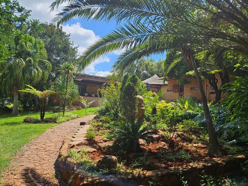 A lush, well-maintained garden featuring a stone pathway, mature trees, and established landscaping surrounding the farm property.